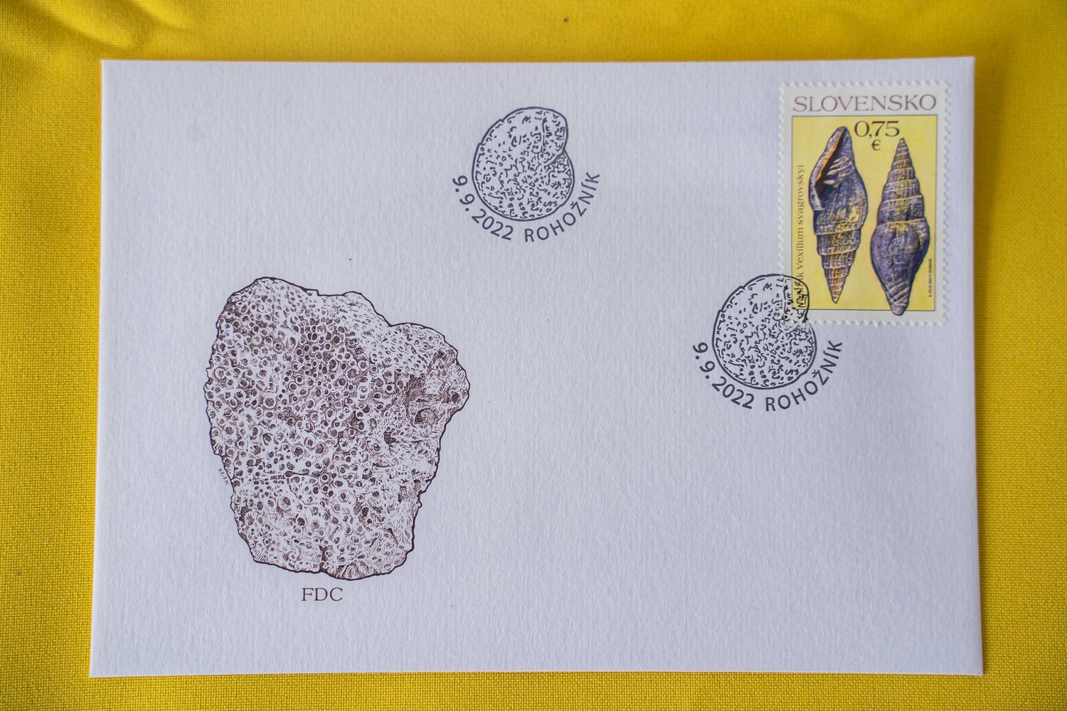 Obálka prvého dňa vydania (FDC) s poštovou známkou ulitníka Vexillum svagrovskyi z lokality Konopiská pri Rohožníku, grafickým zobrazením koralu Heliastrea reussiana zo Štokeravskej vápenky a štylizovaná pečiatka s motívom mikrofosílie - dierkavca